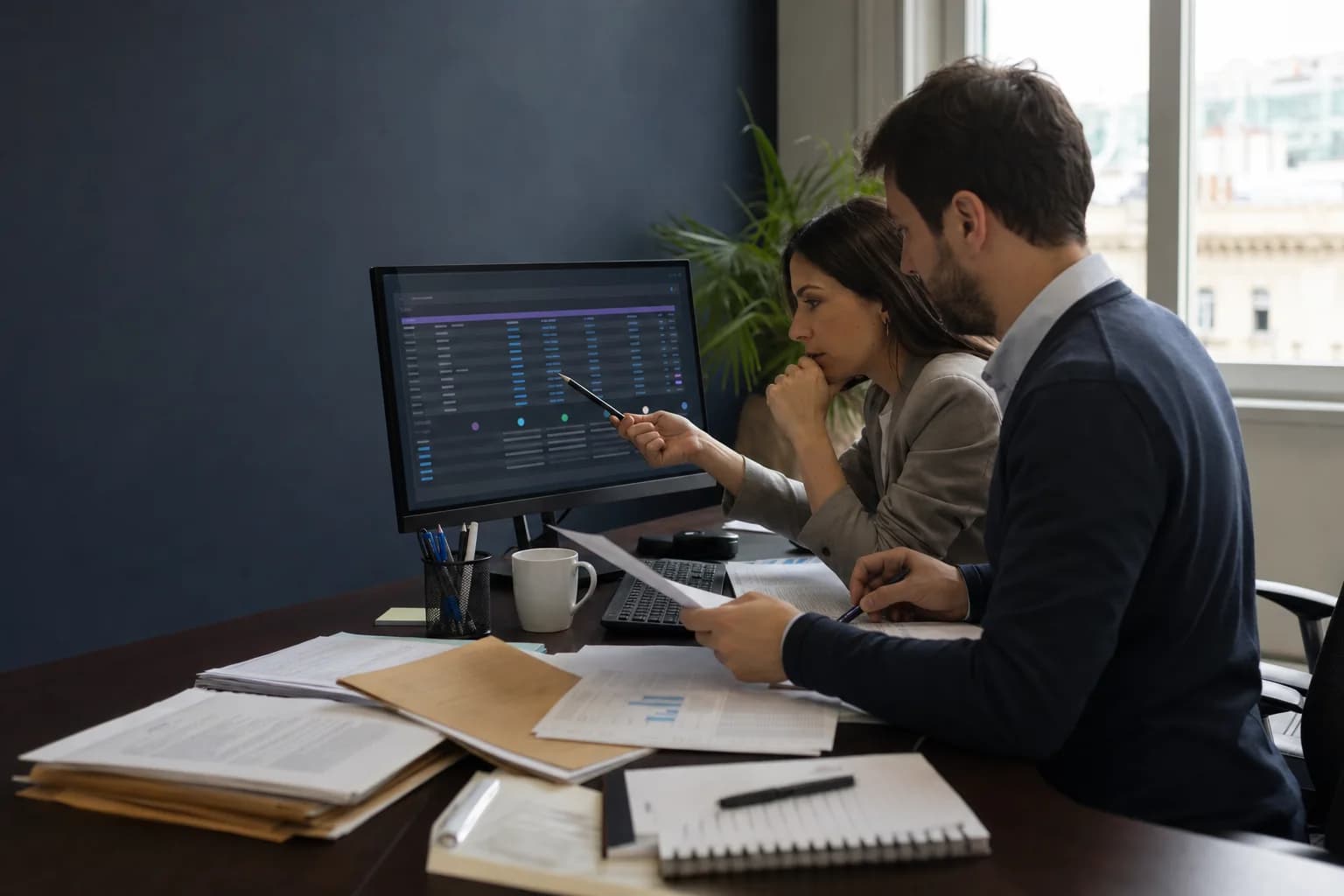 Dos profesionales contables revisan juntos información en una pantalla y documentación impresa